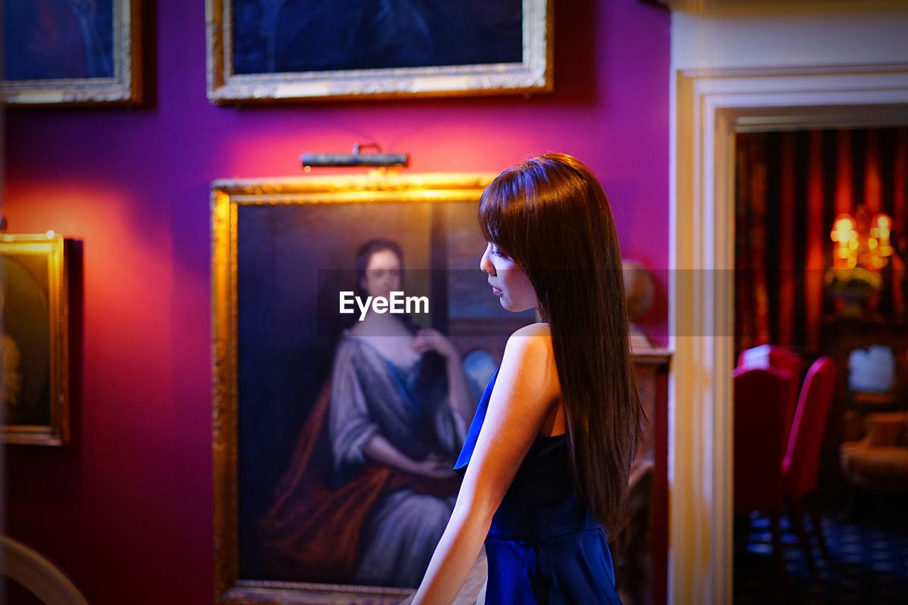 Side view of teenage girl wearing dress standing against paintings