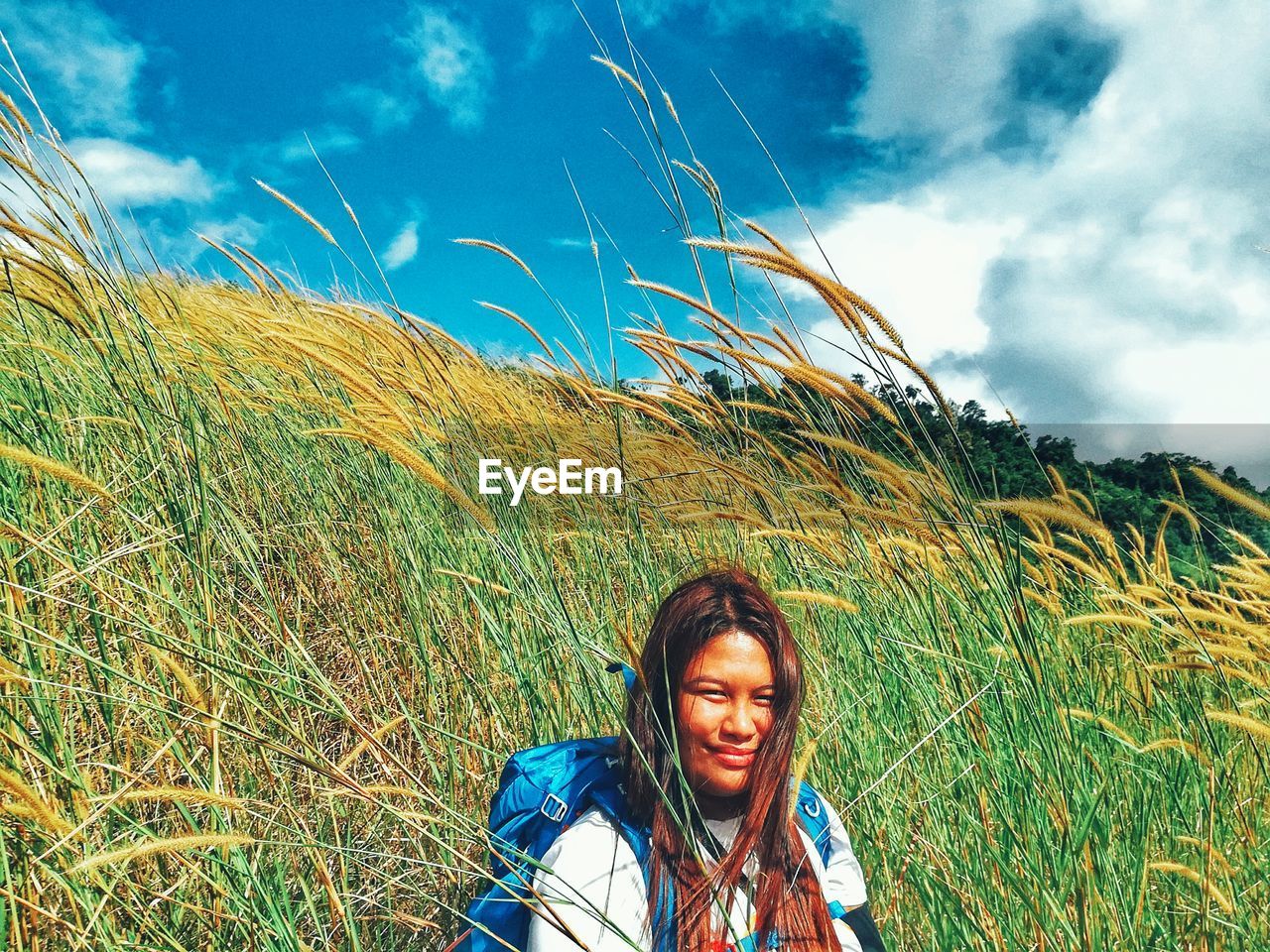 Portrait of smiling young woman standing on field against sky