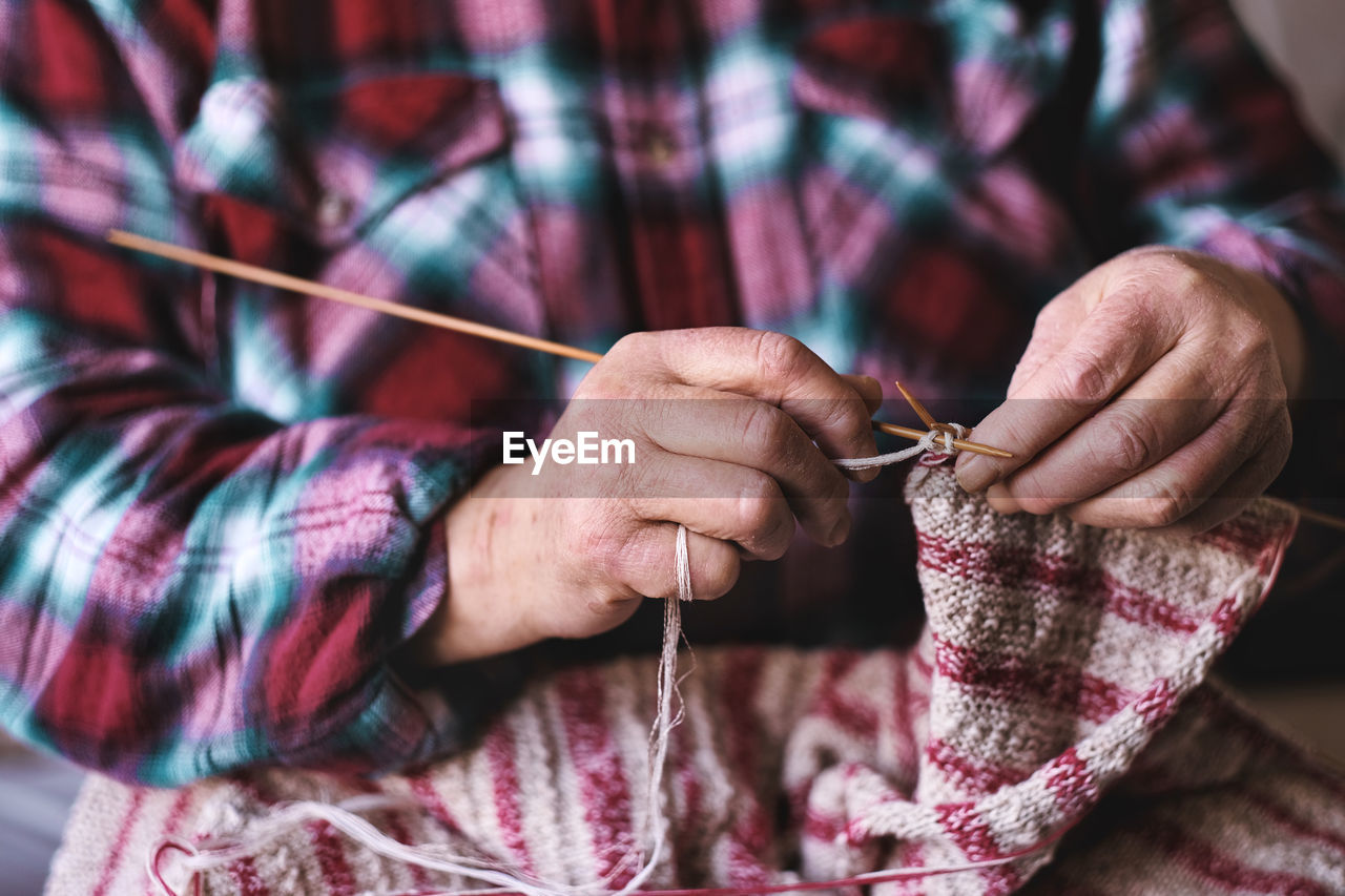 Close up of senior woman hands knitting sweater with needles for grandchild. family bonding and love