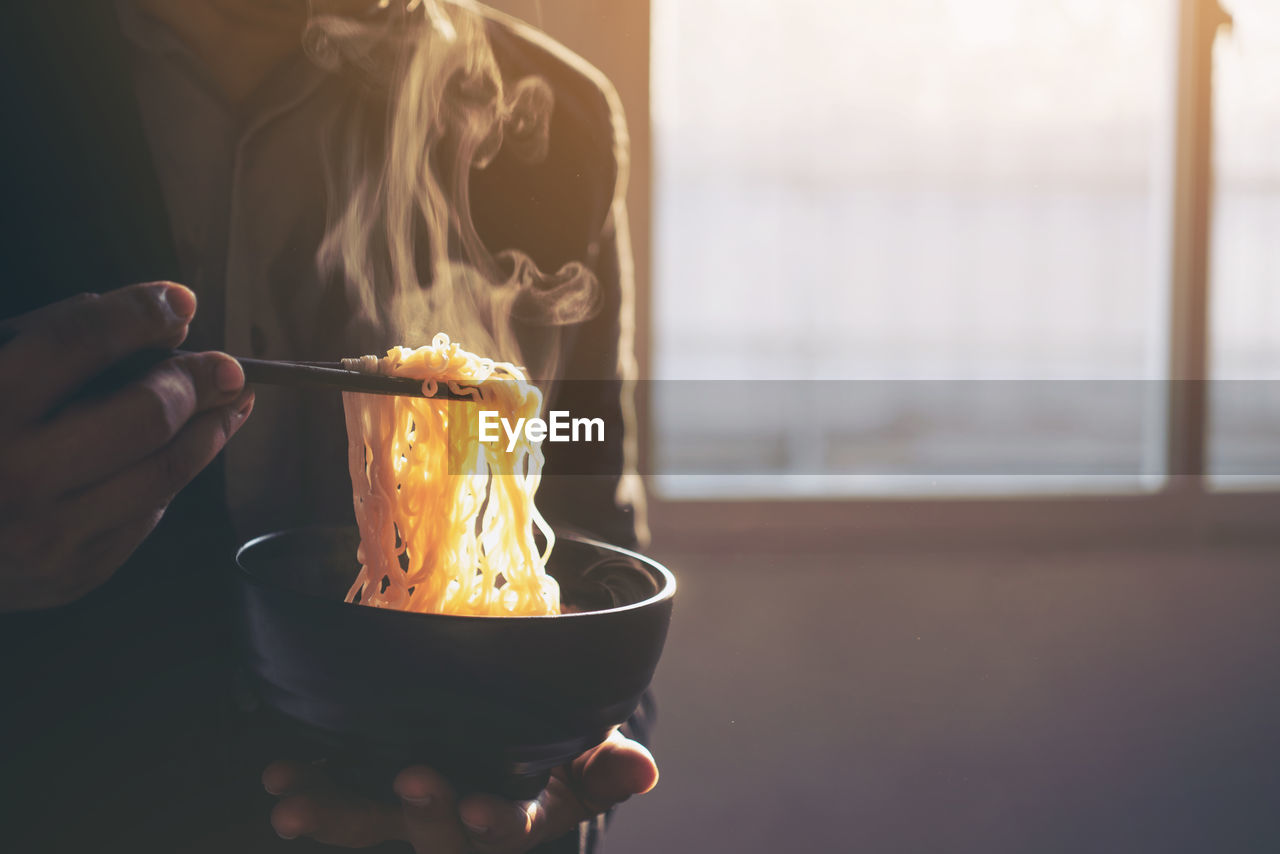 Close-up of hand holding bowl of noodles