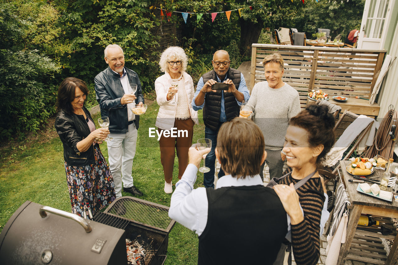 Senior men and women raising toast to party hosts at back yard