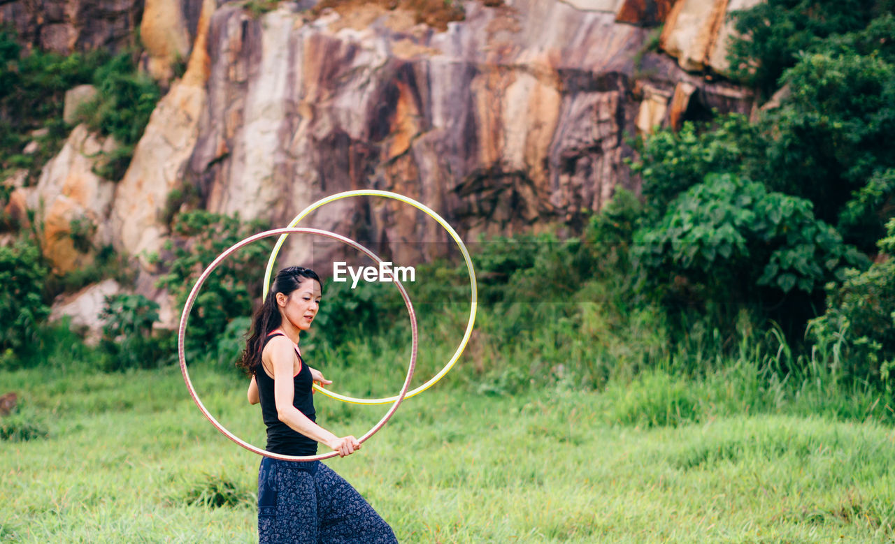 Side view of woman spinning hula hoop while walking on grassy field