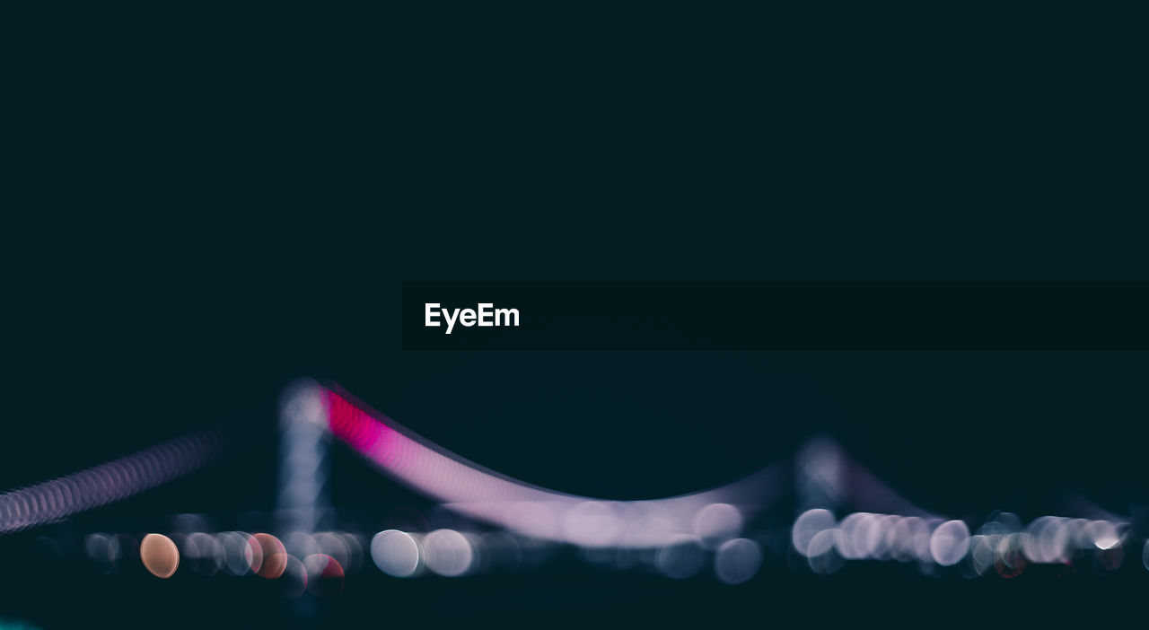 Defocused image of illuminated bridge against clear sky at night