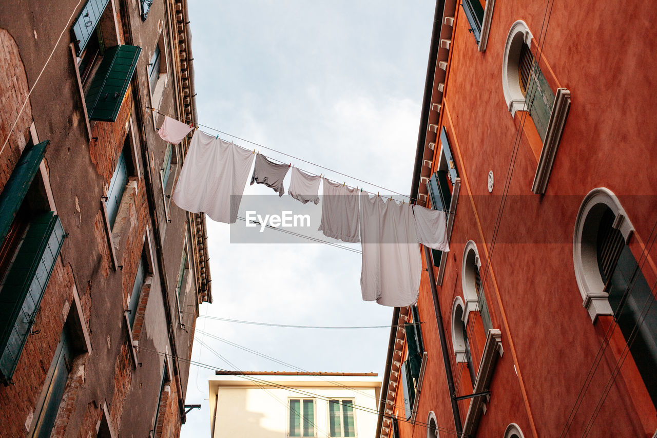 Low angle view of laundry drying amidst buildings against sky