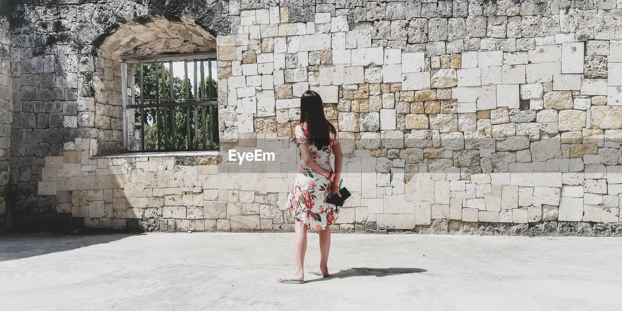 Rear view of woman standing against old wall