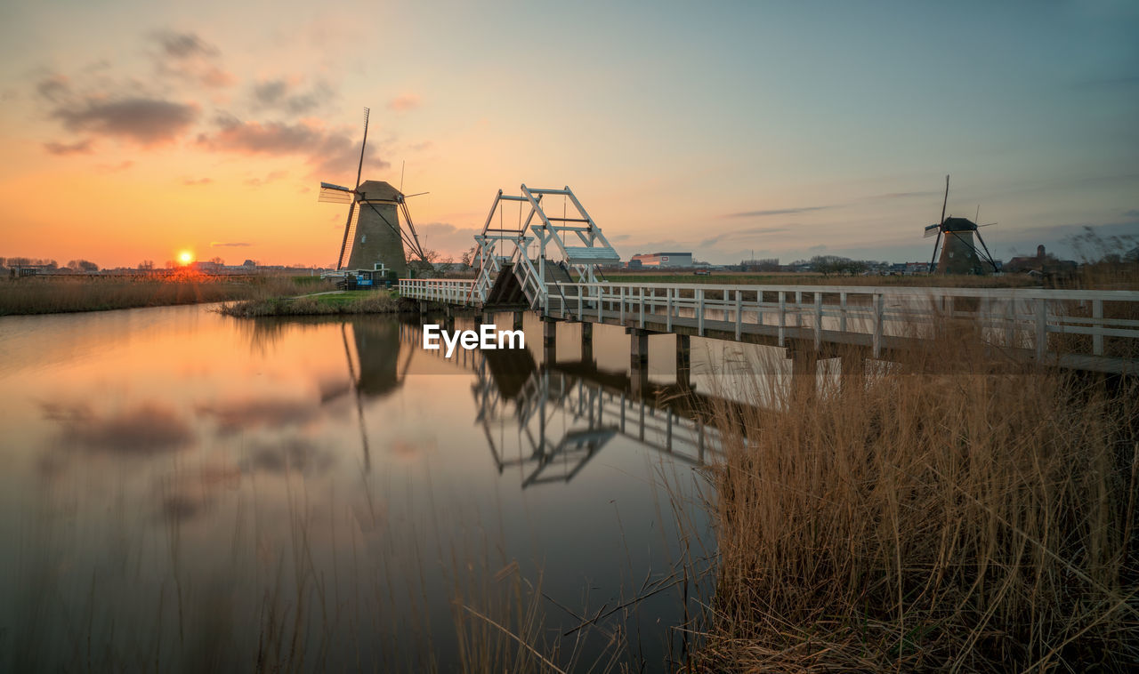 Traditional windmill by river against sky during sunset