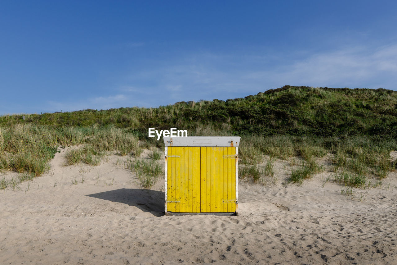 Yellow beach hut on sand against sky