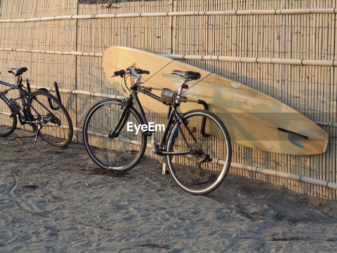 Bicycles with surfboard at beach by wooden fence