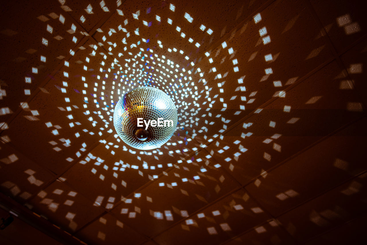 Low angle view of illuminated disco ball hanging from ceiling in nightclub