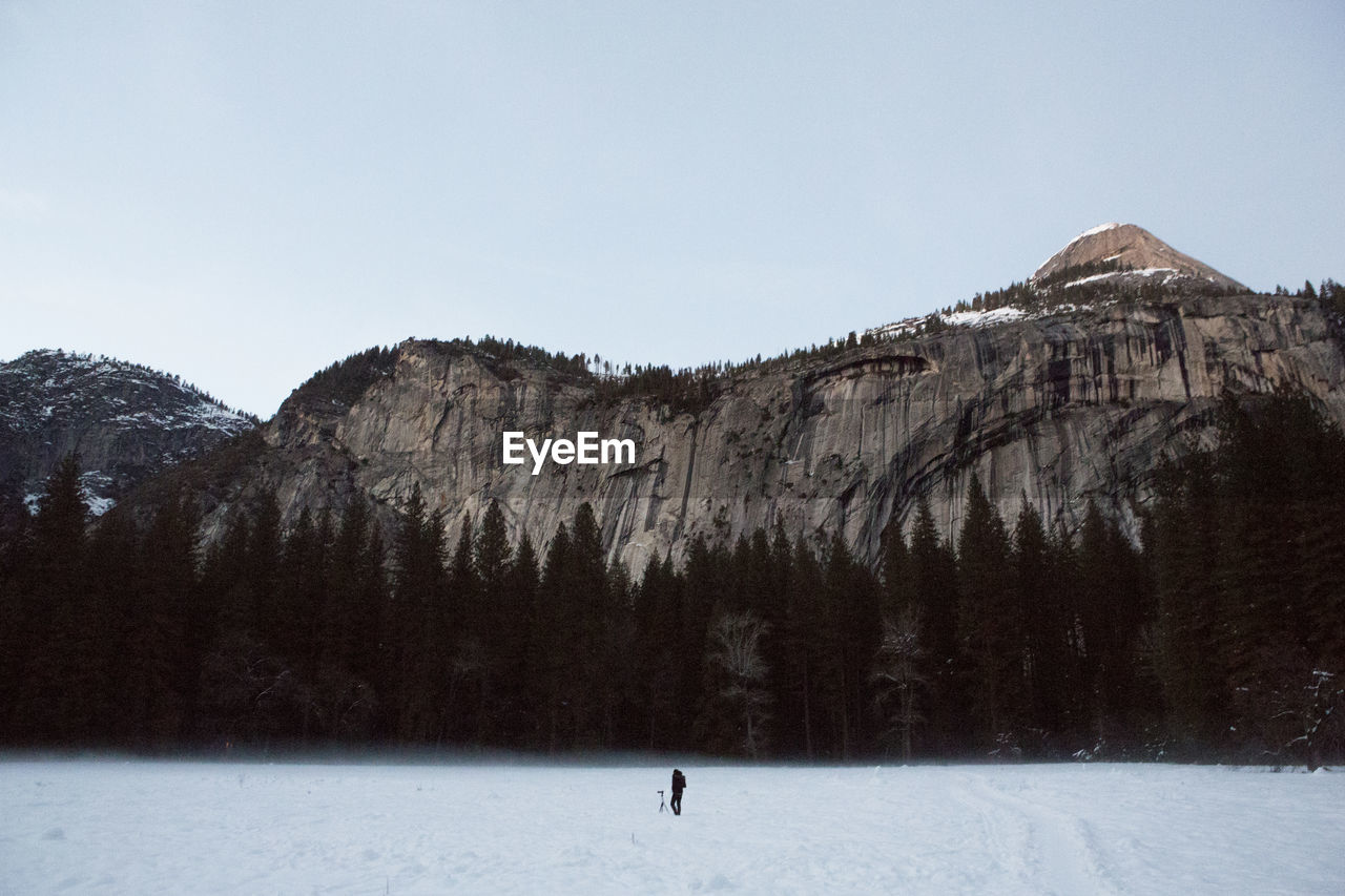 Person on snow covered field against rocky mountain at yosemite national park