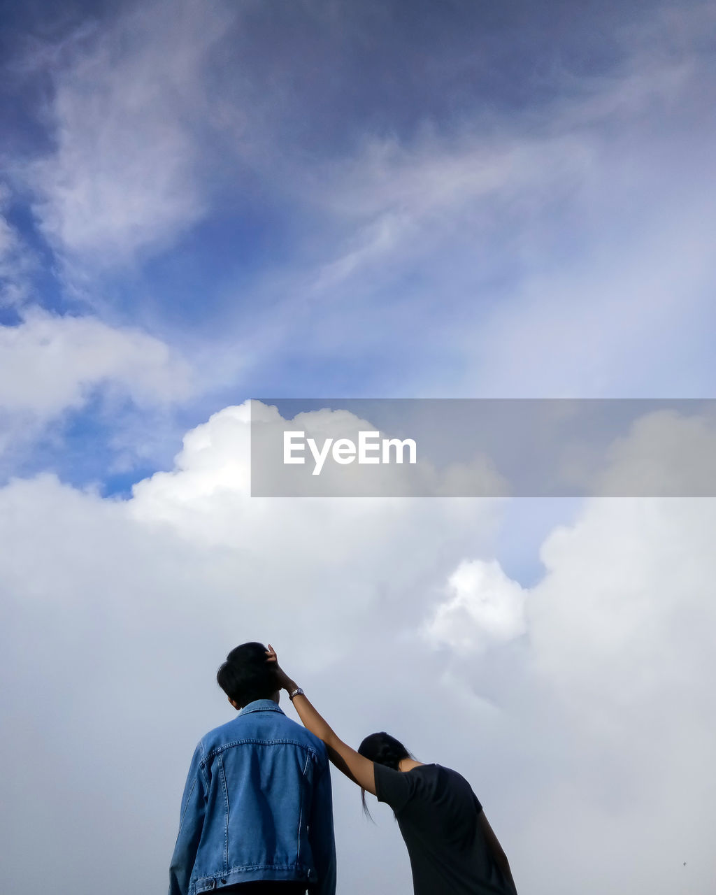 Low angle view of friends standing against cloudy sky