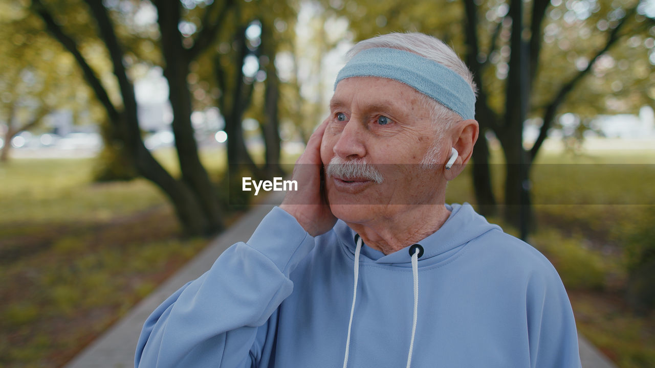 Senior man talking through wireless in ear headphones at park