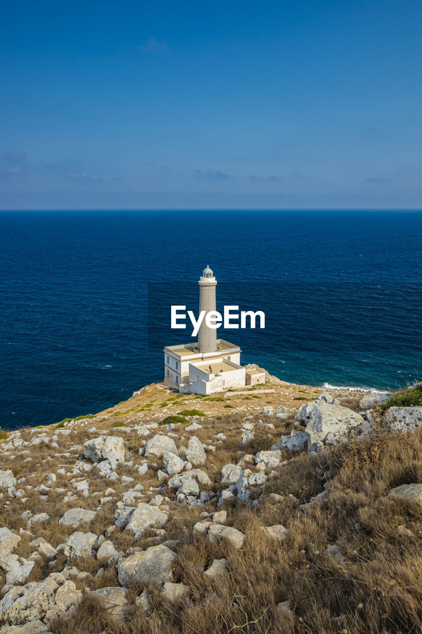 Lighthouse by sea against clear blue sky