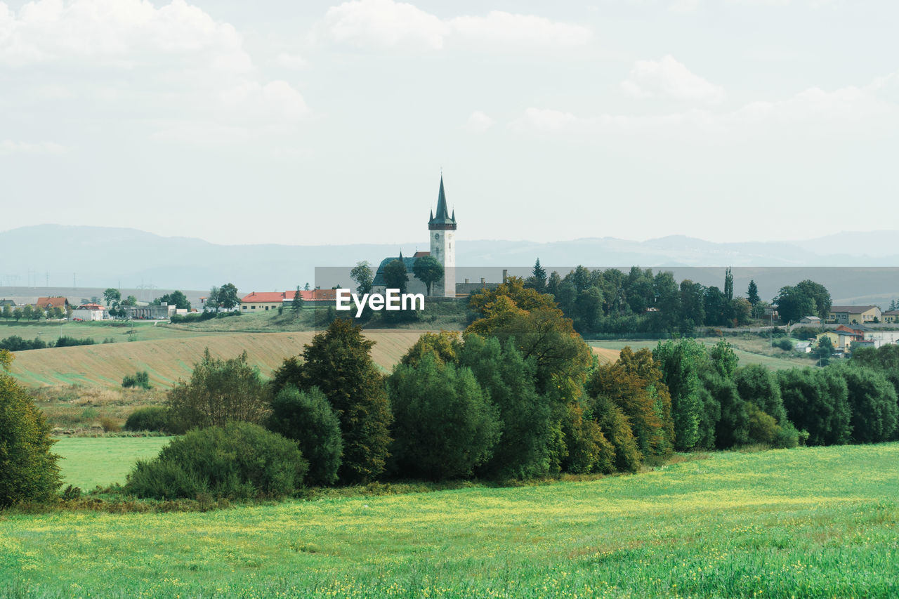 TREES ON FIELD BY BUILDING AGAINST SKY