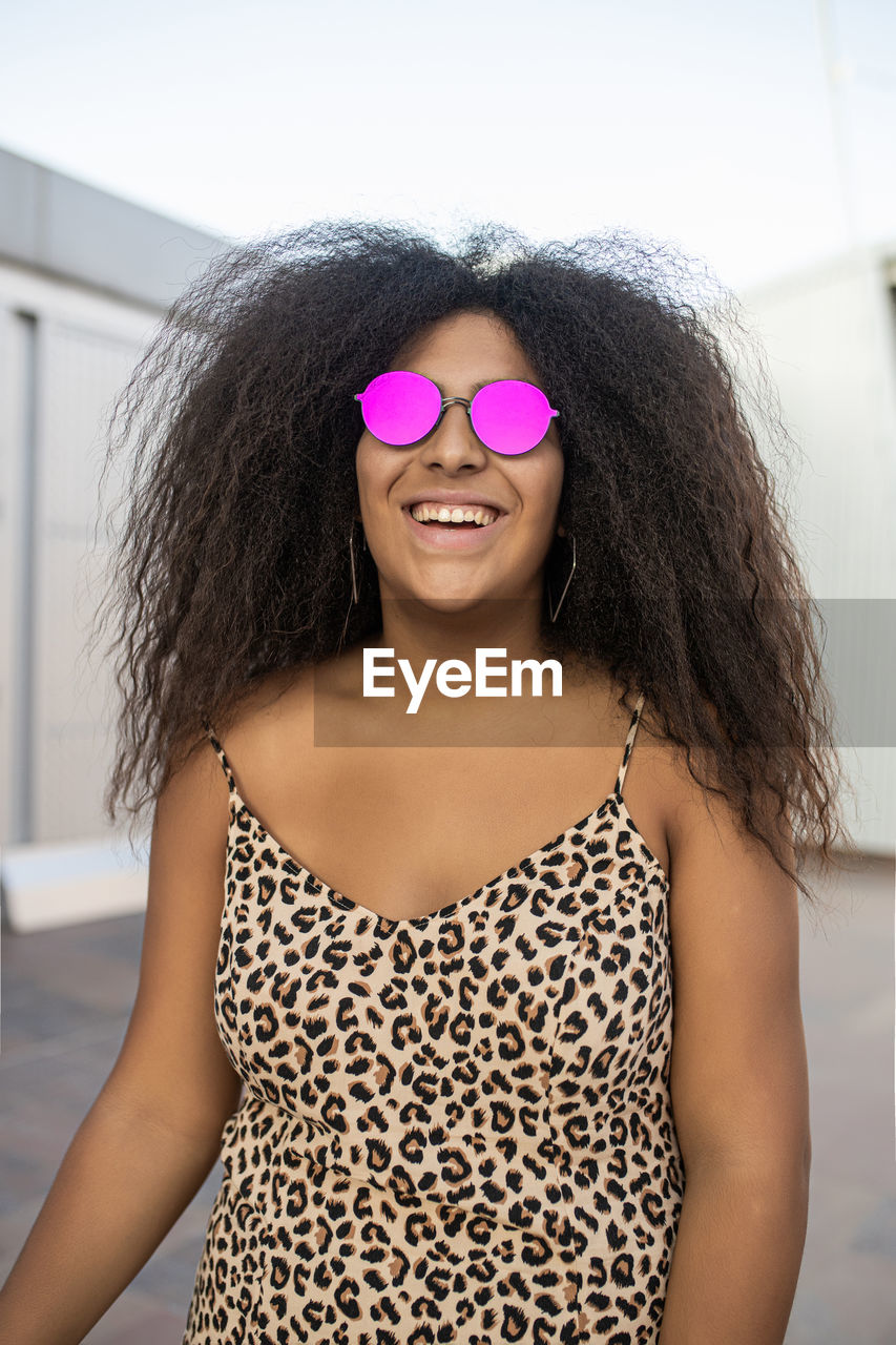 Young and afro woman with sunglasses laughing and smiling while looking at camera