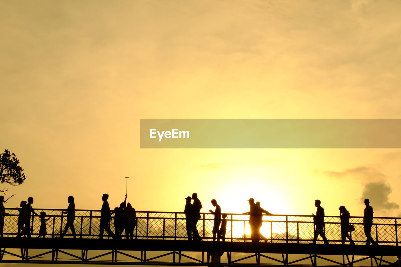 Silhouette people on footbridge against sky during sunset