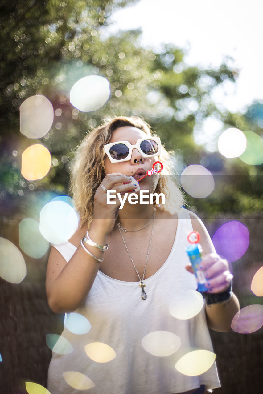 PORTRAIT OF YOUNG WOMAN WITH BUBBLES IN PARK