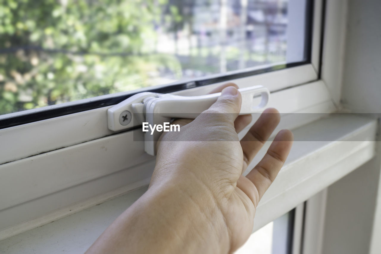 Cropped hand of person opening window at home
