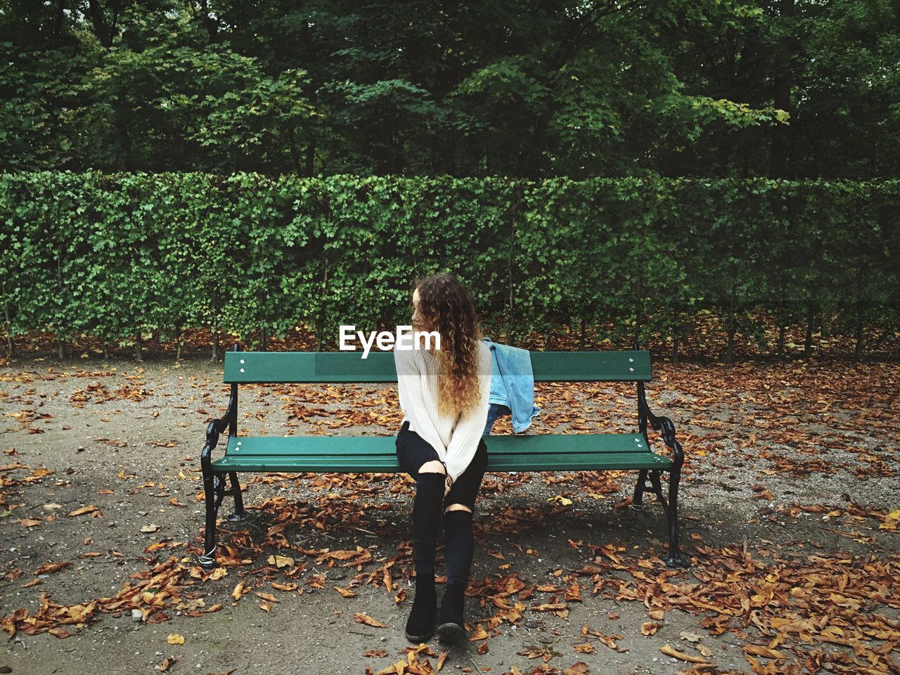 Full length of young woman wearing torn jeans sitting on bench at augarten