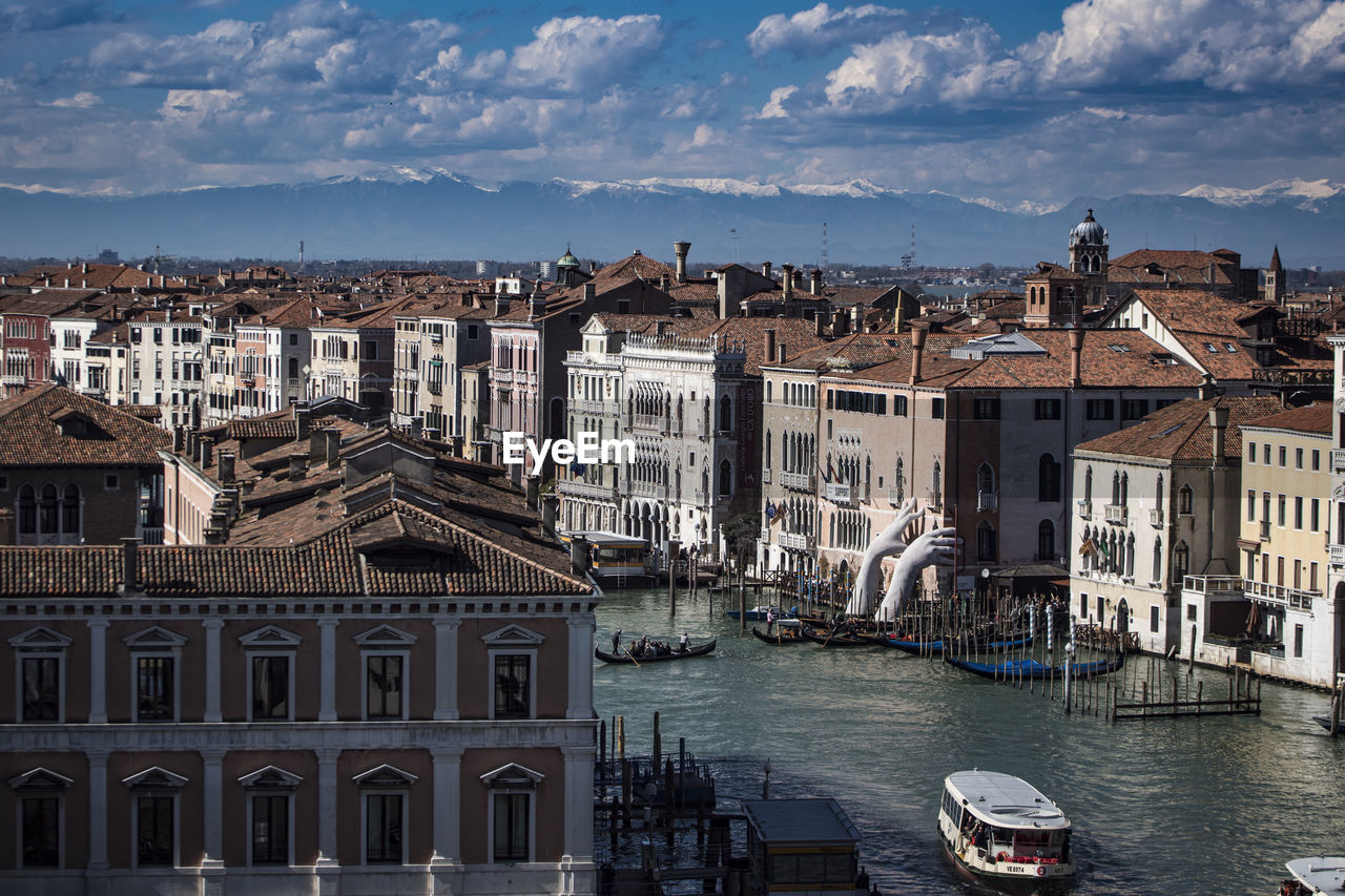 River amidst buildings in city against cloudy sky