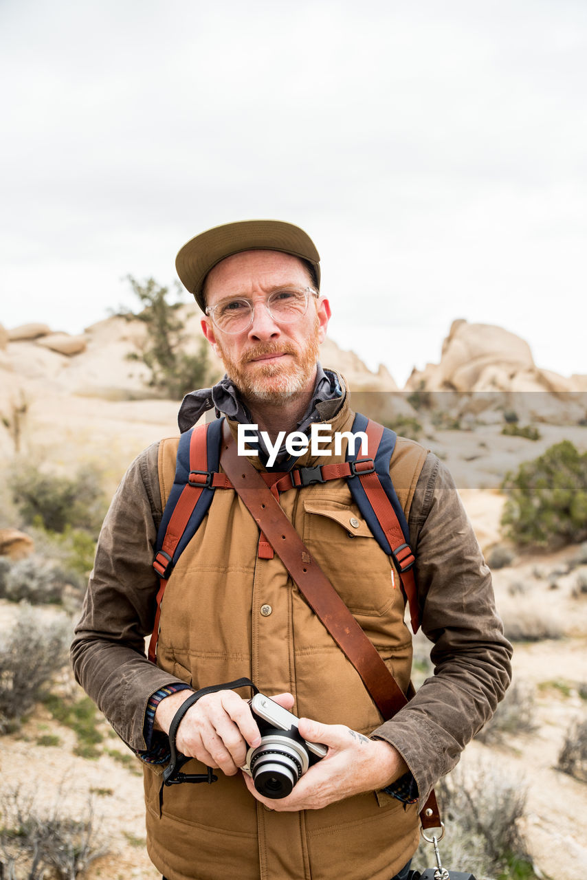 Focused mature man with camera and backpack in desert