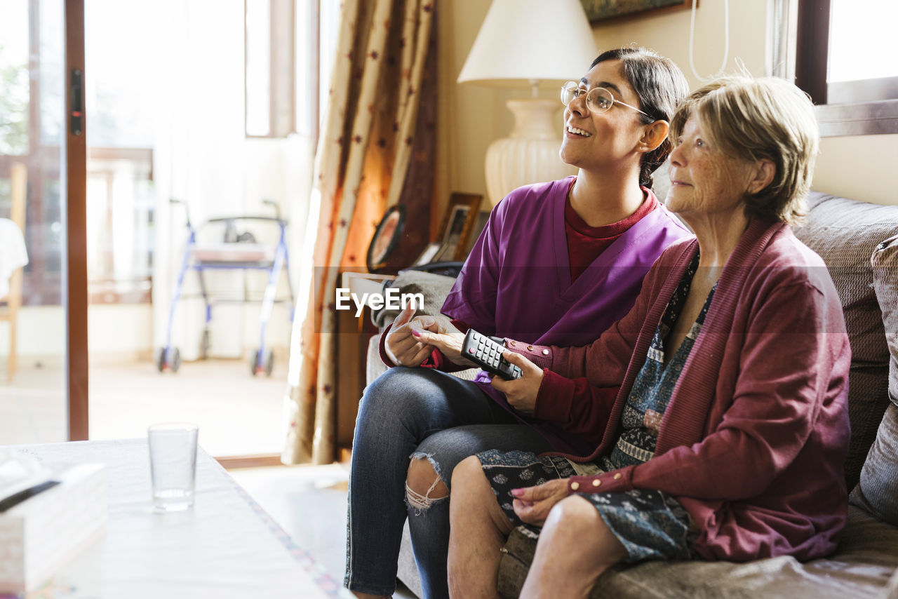 Happy senior woman watching tv with caregiver at home