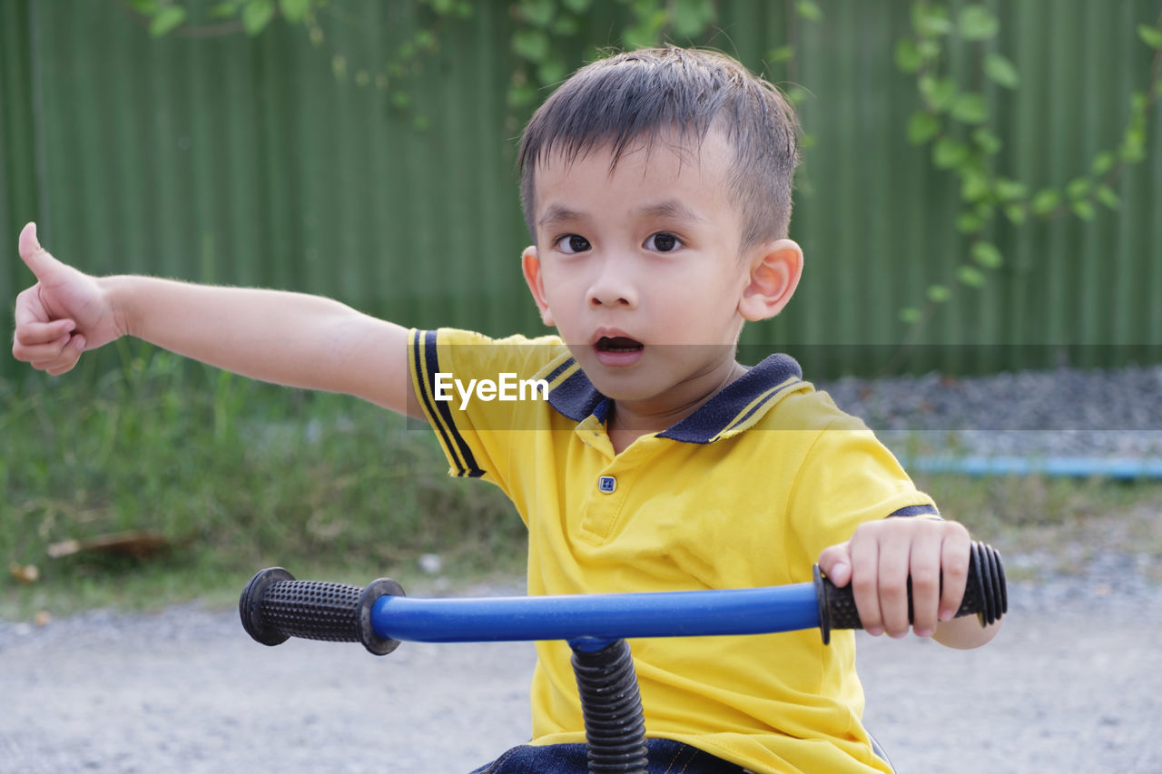 Portrait of cute boy showing thumbs up while riding bicycle on road