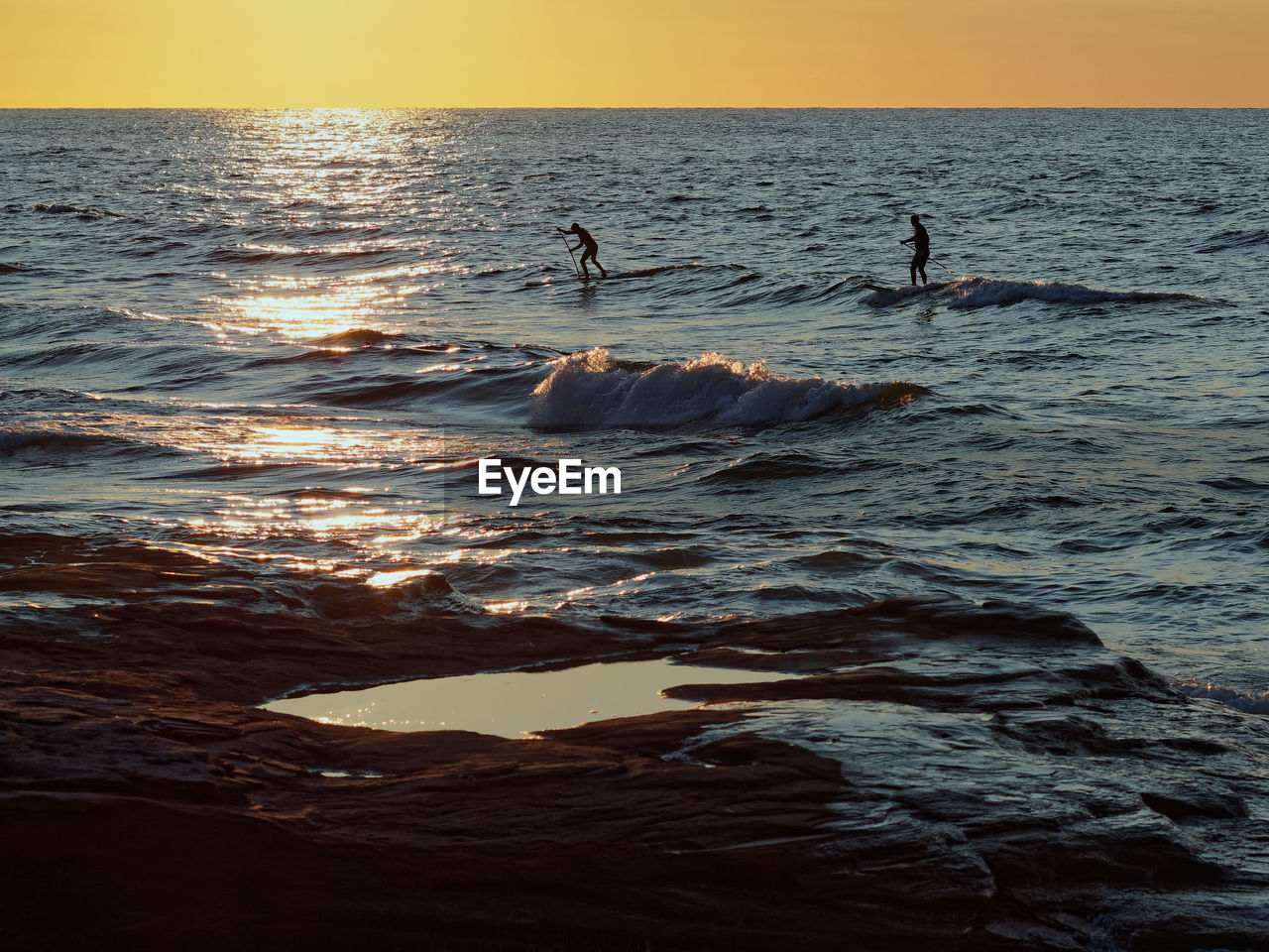 PEOPLE IN SEA AGAINST SKY AT SUNSET