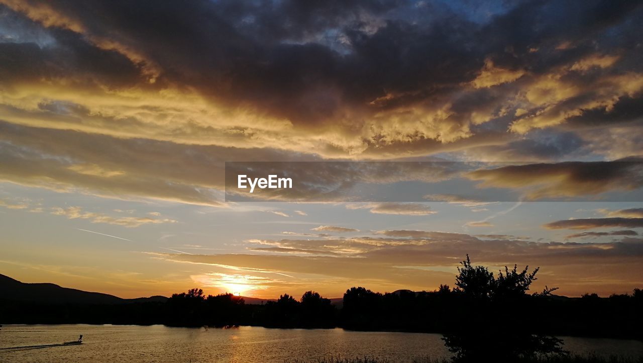 SILHOUETTE TREES BY LAKE AGAINST ORANGE SKY