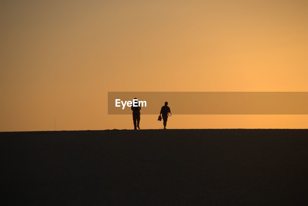 Silhouette of people walking against sky during sunset