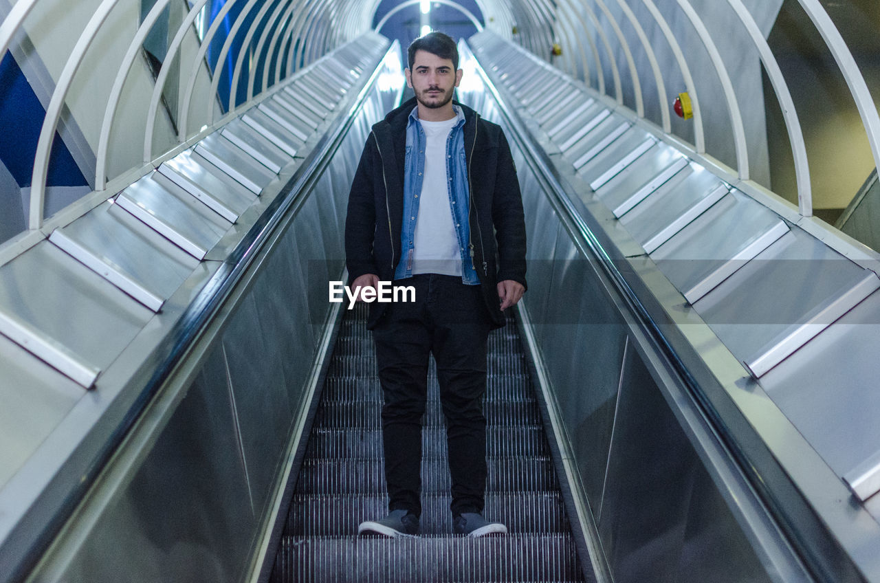 Full length portrait of confident man standing on escalator