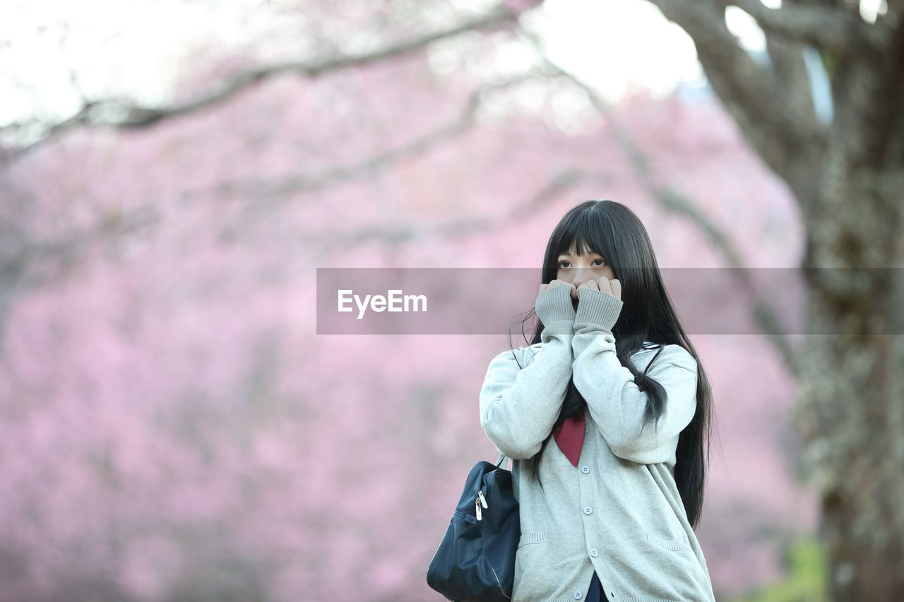 Young woman looking away while standing against pink flowering tree