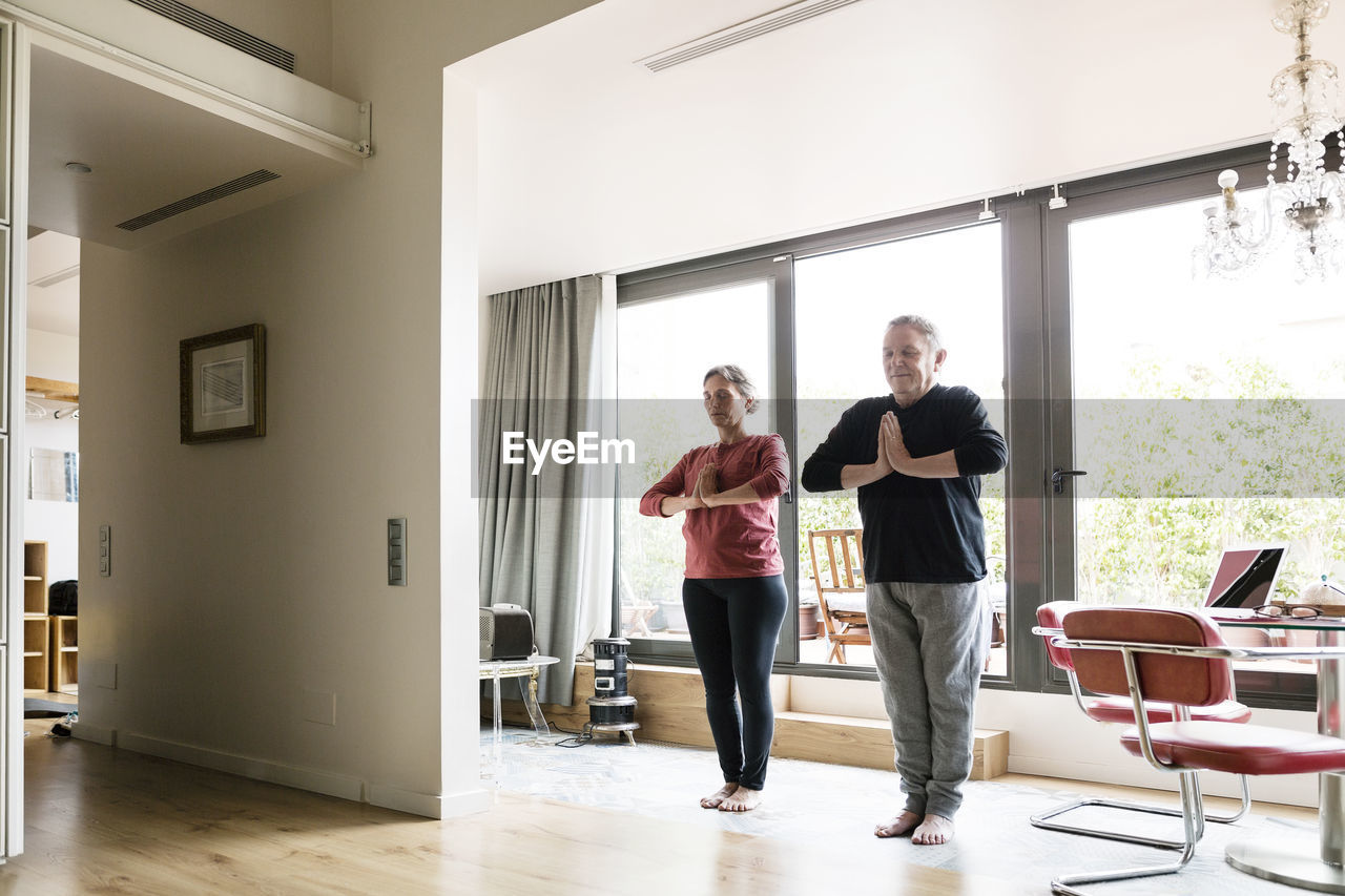 Full length of senior couple practicing yoga at home