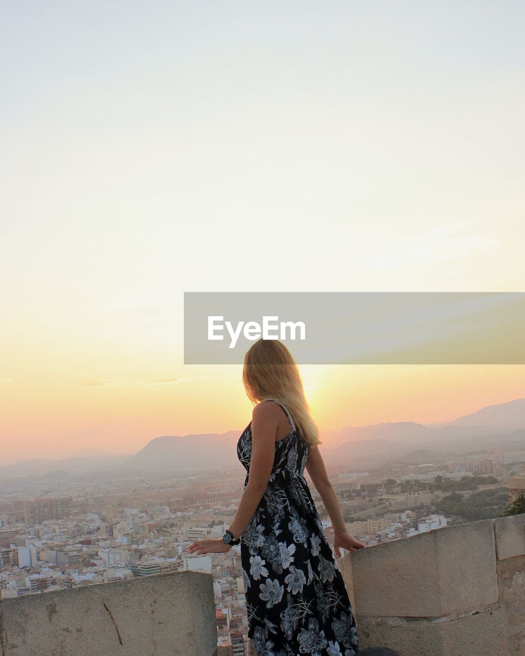 Woman looking at cityscape against sky during sunset