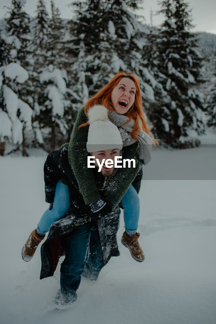 Man carrying woman on back on snow covered land