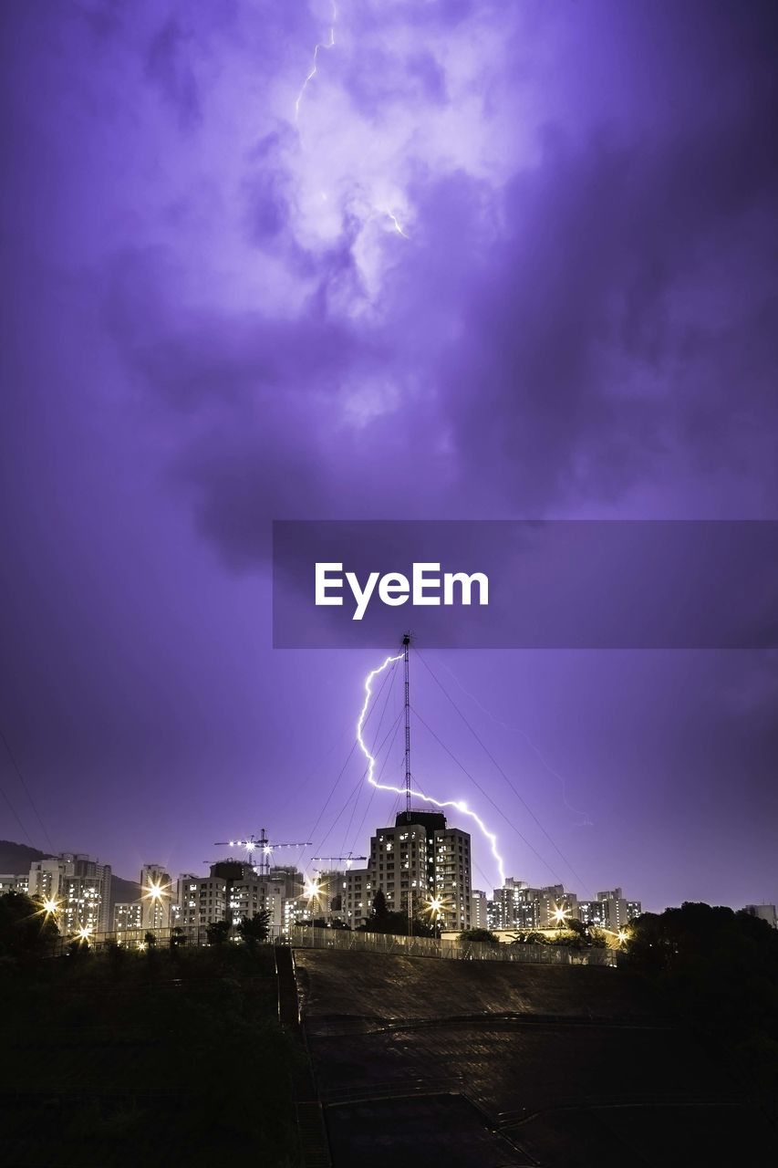 Idyllic shot of lightning over illuminated city against purple sky