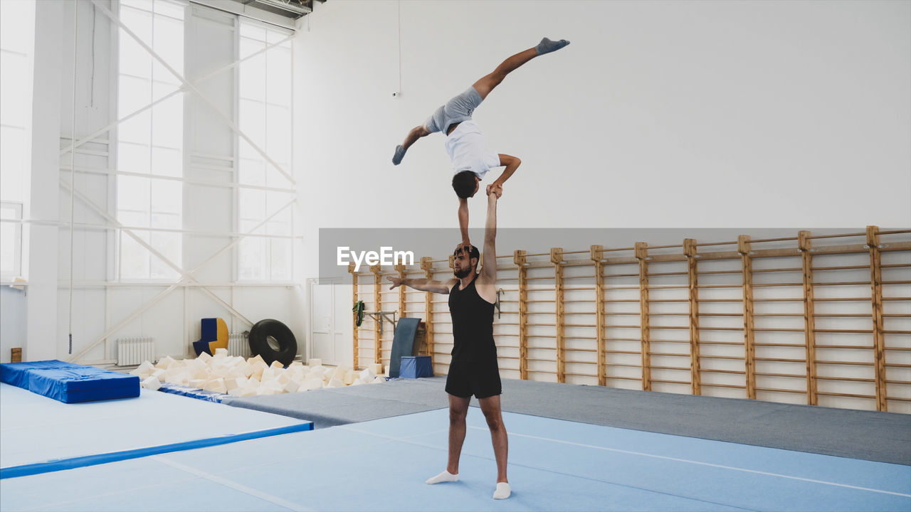 Instructor with teenage boy practicing gymnastics in club