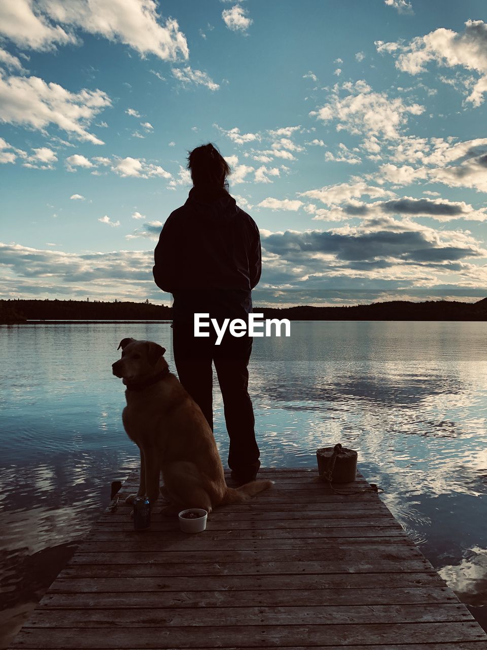 REAR VIEW OF MAN WITH DOG ON PIER AT SUNSET