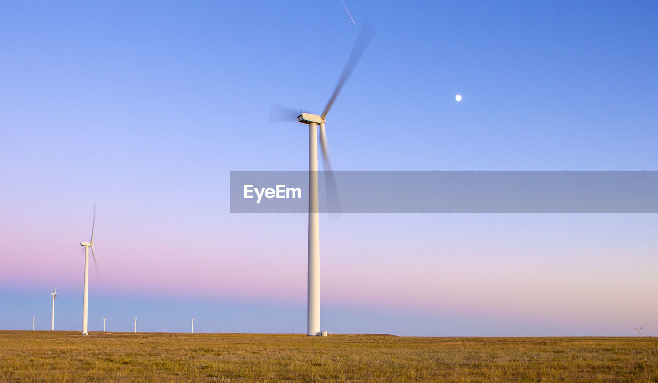 Wind turbines in field against blue sky at dusk