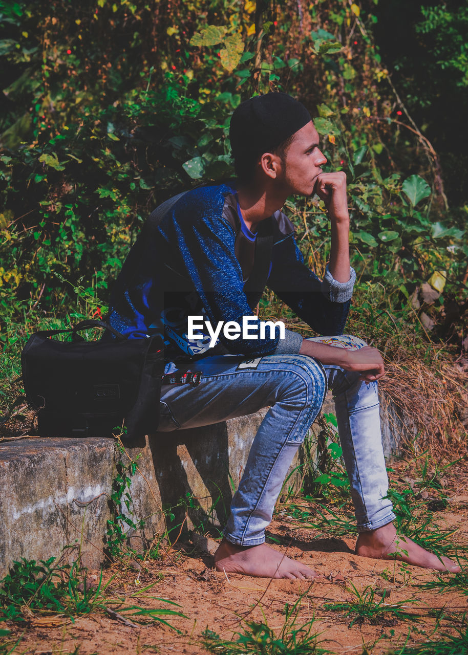 Young man looking away while sitting on bench