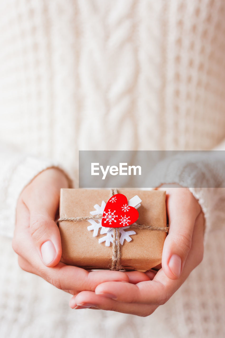 Woman in knitted sweater holds present. gift  with red heart. diy way to pack christmas presents. 