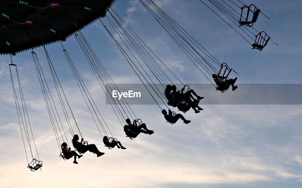 Low angle view of silhouette chain swing ride against sky