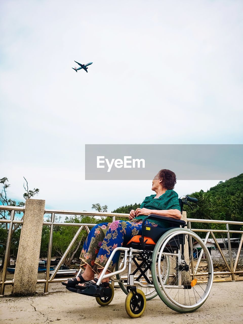 Woman sitting on wheelchair against airplane in sky