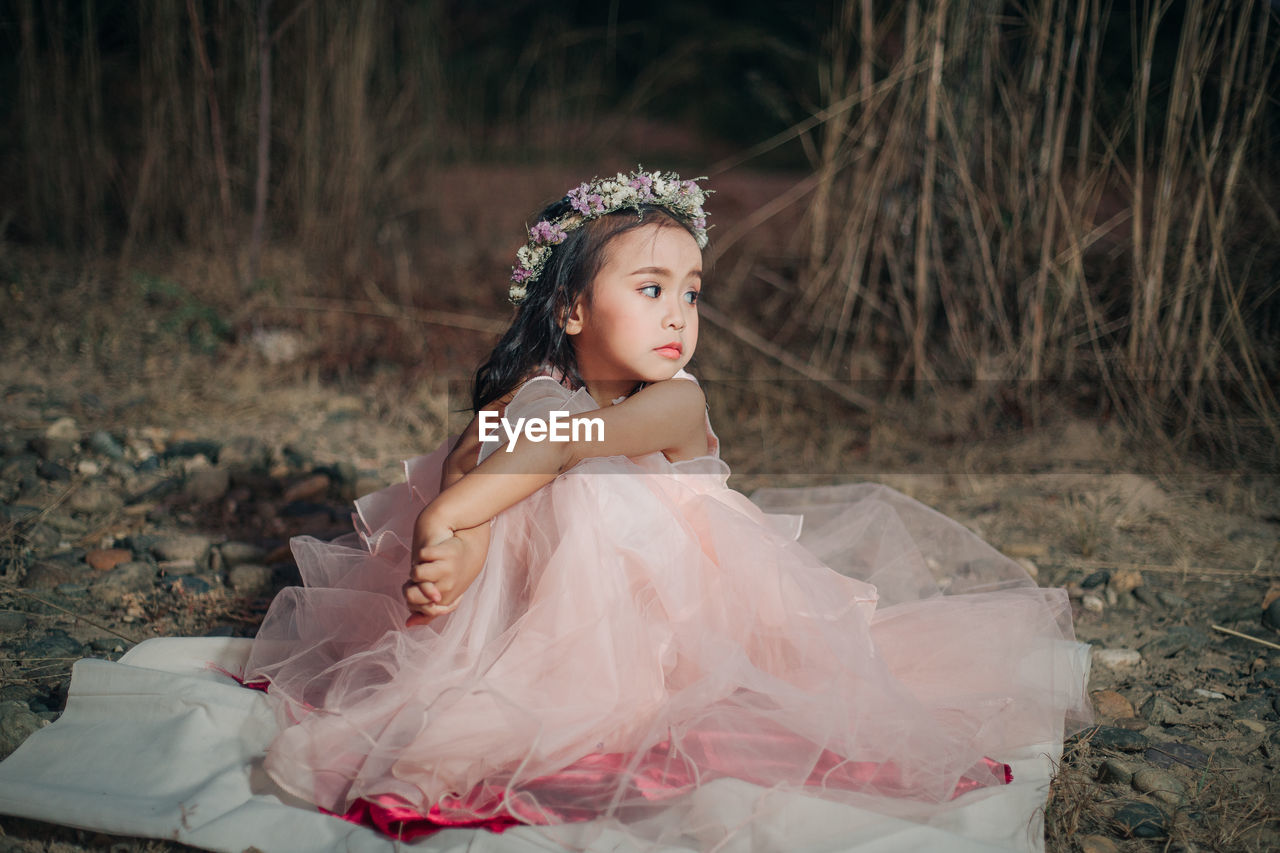 Young woman looking away while sitting on land