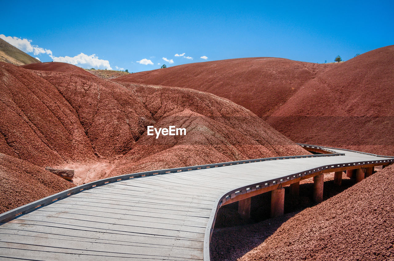 Empty boardwalk amidst mountains against sky