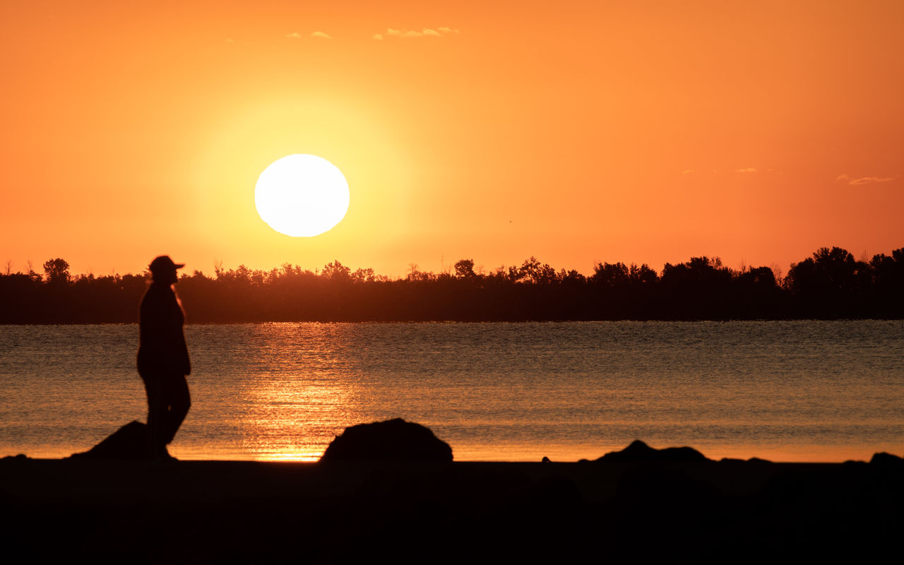 sunset, silhouette, sky, water, horizon, orange color, beauty in nature, dawn, nature, afterglow, sun, sea, one person, scenics - nature, tranquility, evening, beach, land, tranquil scene, adult, sunlight, leisure activity, lifestyles, men, reflection, idyllic, full length, outdoors, vacation, backlighting, relaxation, standing, landscape, trip, cloud, holiday, ocean, activity, travel destinations, person, rock, environment, travel, back lit, non-urban scene