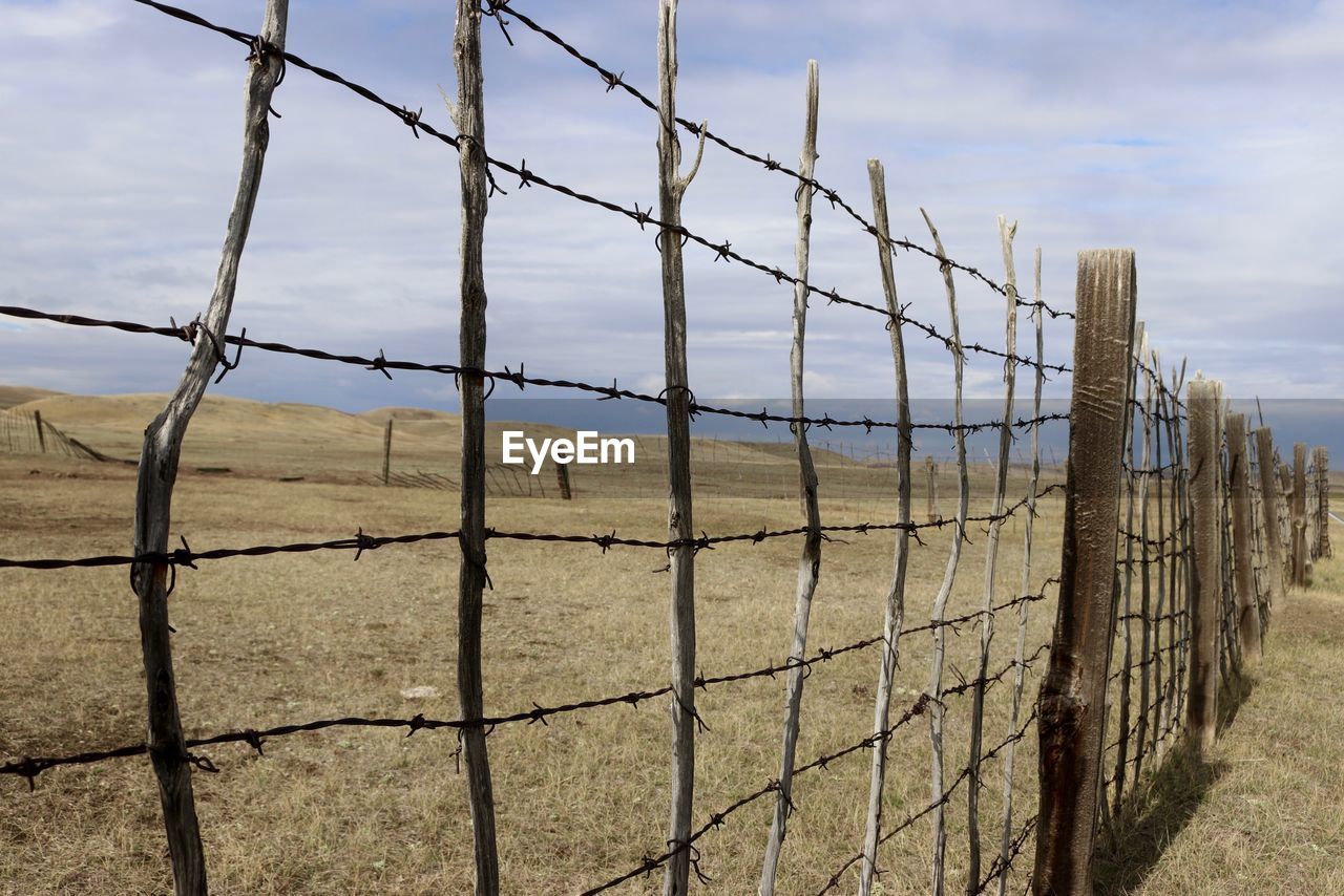 BARBED WIRE FENCE ON FIELD AGAINST SKY SEEN THROUGH CHAINLINK