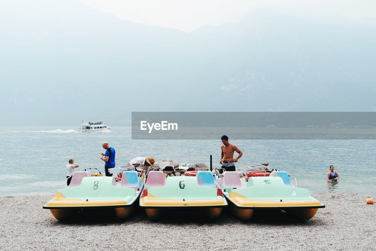 REAR VIEW OF PEOPLE SITTING ON BOAT IN SEA