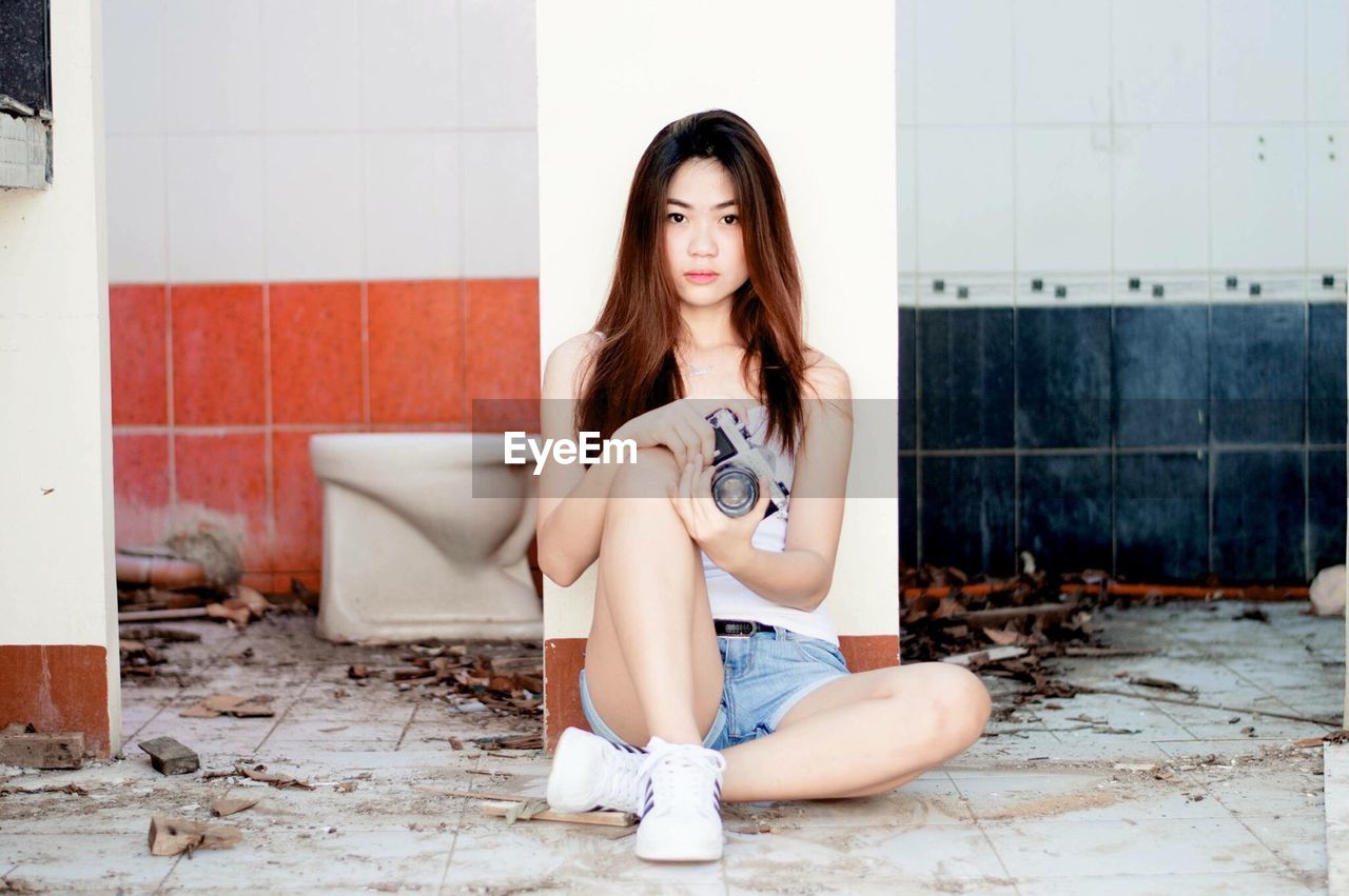 PORTRAIT OF YOUNG WOMAN SITTING ON WALL