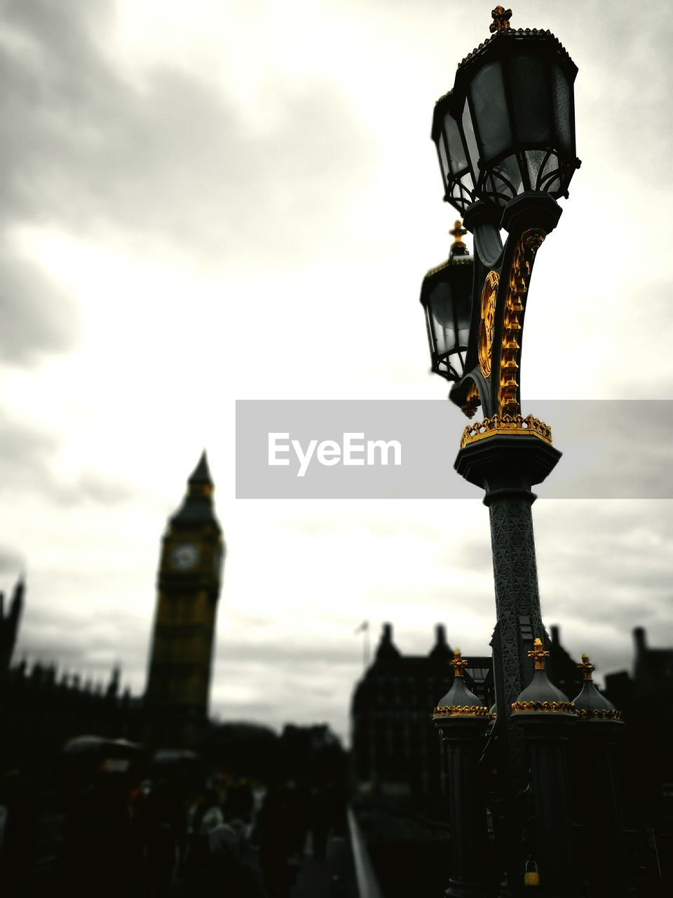 Street light at westminster bridge by big ben against cloudy sky during sunset